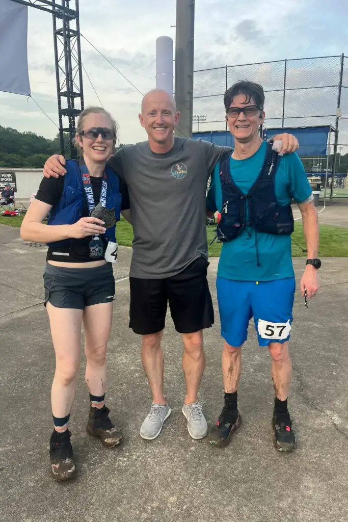 Man and woman drenched in sweat at the finish line hugging the race director of the Night Howler 50.
