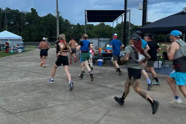 Group of people in trail running gear running from the start line of a race at dusk.